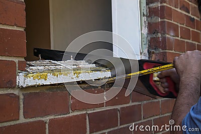Workman using a saw and crowbar to remove an old wooden window frame Stock Photo