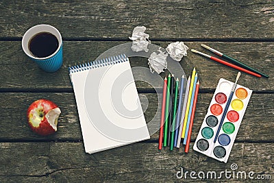 Workplace of the artist. Never give up. Cup of hot coffee, notepad with blank sheet of paper, colored pencils, paint, brushes. Stock Photo