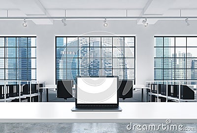 A workplace in a bright modern loft open space office. A working desk is equipped with a modern laptop with white copy space in th Stock Photo