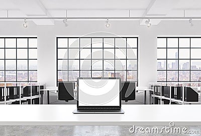 A workplace in a bright modern loft open space office. A working desk is equipped with a modern laptop with white copy space in th Stock Photo