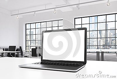 A workplace in a bright modern loft open space office. A working desk is equipped with a modern laptop with white copy space in th Stock Photo