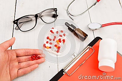 Workplace of doctor. Pills in hand, red stethoscope, clipboard and glasses on white wooden table Stock Photo