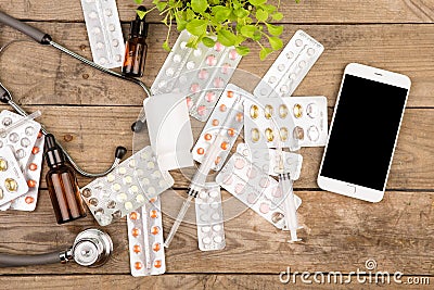 Pills, syringe, stethoscope and smart phone on brown wooden desk Stock Photo