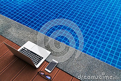 Workplace at the resort. Laptop and smartphone glasses near blue swimming pool. Modern Gadgets. Stock Photo