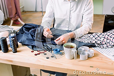 Workplace of seamstress. Crop image of dressmaker hands sewing a button. Buttons, materials for pants, pattern, scissors Stock Photo