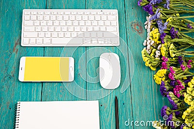 Workplace with wireless slim keyboard, mouse, smart phone, notepad, pencil, colorful flowers on blue wooden desk Editorial Stock Photo