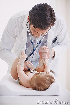 He works so well with his little patients. A male doctor examining an infant girl with his stethoscope. Stock Photo