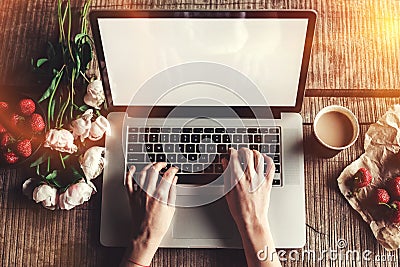 Workspace with girl`s hands, laptop computer, bouquet of peonies flowers, coffee, strawberries, smartphone on rough wooden table. Stock Photo