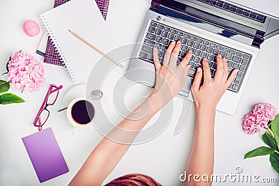 Workspace with girl`s hands on laptop keyboard, notebook, glasses, cup of coffee and wisteria flowers on white background. Top vi Stock Photo