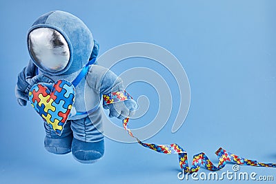 World Autism awareness day background. Blue plush astronaut toy with puzzle heart, autism symbol, on blue background Stock Photo