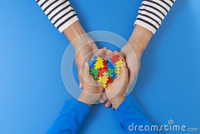 World autism awareness day concept. Female and child hands holding puzzle heart on light blue background Stock Photo