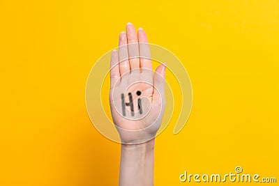 World hello day. Raised female hand with the inscription Hi on the palm. Yellow background. Copy space Stock Photo
