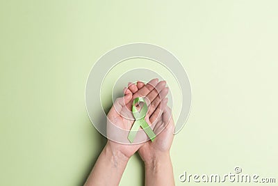 World mental health day concept. Green awareness ribbon in female hands on a green background Stock Photo