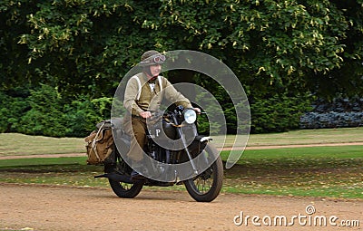 World War 2 despatch rider in uniform on classic motorcycle riding in park land. Editorial Stock Photo