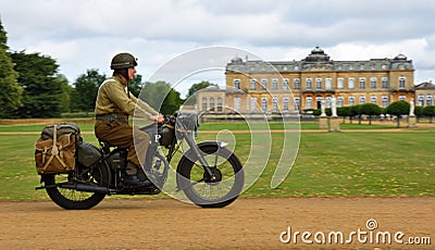 World War 2 despatch rider in uniform on classic motorcycle riding past stateley home. Editorial Stock Photo