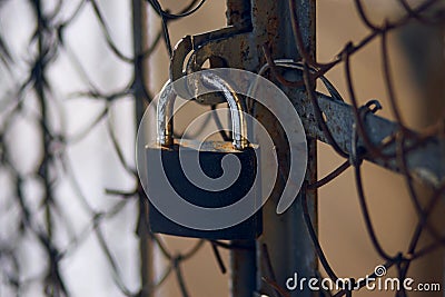 A worn-out lock covering an old rusty gate with a metal mesh Stock Photo