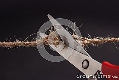 Worn rope ready to break, with scissors on black background Stock Photo