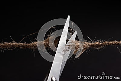 Worn rope ready to break, with scissors on black background Stock Photo