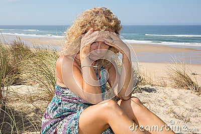 Worried blond girl on the beach sitting on the sand Stock Photo