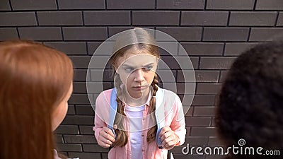 Worried caucasian schoolgirl looking at elder students, communication conflict Stock Photo