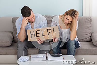 Worried Couple Holding Help Sign While Calculating Bills Stock Photo