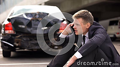 Worried man talking on phone outdoors broken auto background, traffic collision Stock Photo