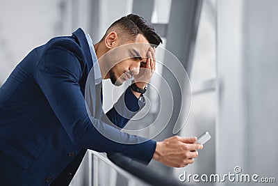 Worried middle-eastern businessman looking at smartphone screen while waiting at airport terminal Stock Photo