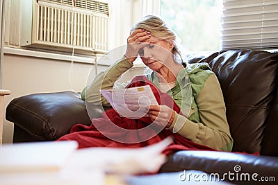 Worried Senior Woman Sitting On Sofa Looking At Bills Stock Photo