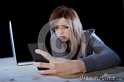 Worried teenager using mobile phone and computer as internet cyber bullying stalked victim abused Stock Photo