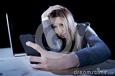 Worried teenager using mobile phone and computer as internet cyber bullying stalked victim abused Stock Photo