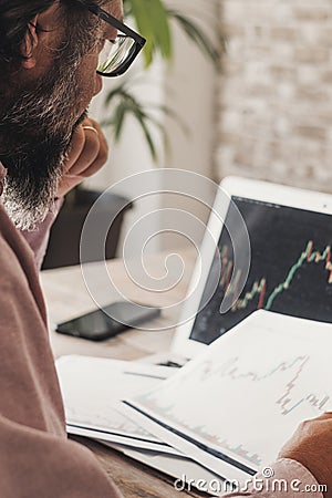 Worried and thoughtful man study stock exchange crypto charts on paper and computer display. Concept of economy and money Stock Photo