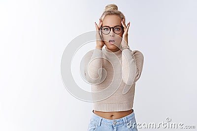 Worried and troubled young panicking woman standing anxious open mouth and gasping perplexed, grabbing head with hands Stock Photo