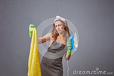 Worried unhappy woman looking at yellow clothes with damage at studio. Stressed housewife holds an iron. Stock Photo