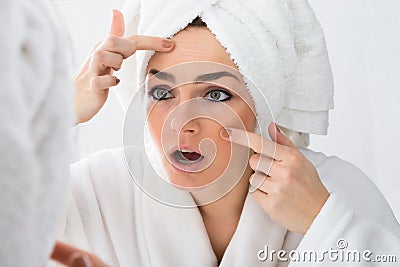 Worried woman looking at pimple on face Stock Photo