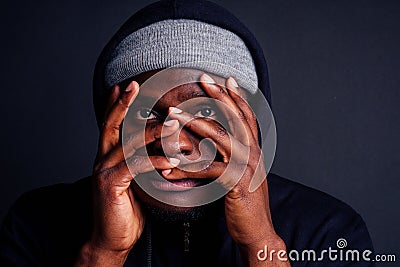 Worried young african american mele wearing gray hat and black hoody with hood hiding from the rapist s blow attacker Stock Photo