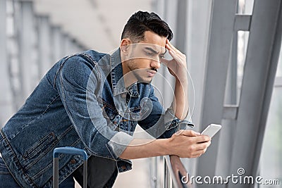 Worried young arab man looking at smartphone screen while waiting at airport Stock Photo