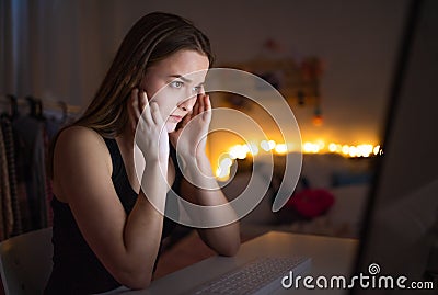 Worried young girl with computer sitting indoors, internet abuse concept. Stock Photo