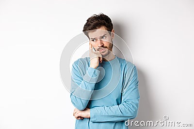 Worried young man with beard in sweatshirt, looking away pensive and thinking, standing troubled against white Stock Photo