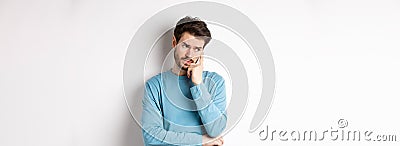 Worried young man with beard in sweatshirt, looking away pensive and thinking, standing troubled against white Stock Photo