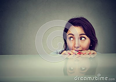 Worried young woman looking at something peeking from under the table Stock Photo