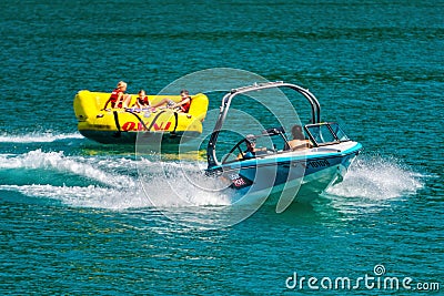 WORTHERSEE, AUSTRIA - AUGUST 08, 2018: Happy young people, on inflatable attractions, drive behind a motorboat on the lake. Editorial Stock Photo