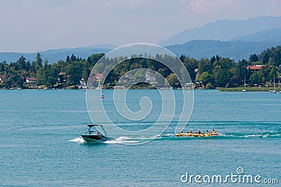 WORTHERSEE, AUSTRIA - AUGUST 08, 2018: Happy young people, on inflatable attractions, drive behind a motorboat on the lake Editorial Stock Photo
