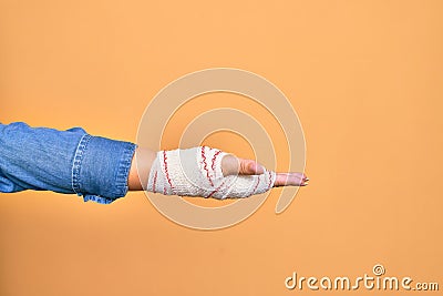 Wounded hand of caucasian young woman cover with bandage doing give me gesture with open empty palm over isolated yellow Stock Photo