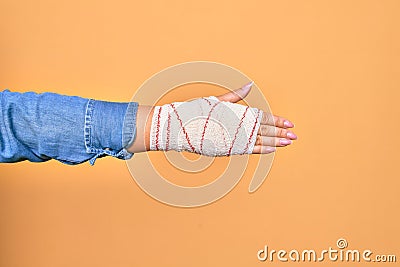 Wounded hand of caucasian young woman cover with bandage doing handshake gesture over isolated yellow background Stock Photo