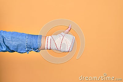 Wounded hand of caucasian young woman cover with bandage doing ok sign with thumb up over isolated yellow background Stock Photo