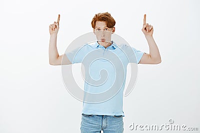 Wow, it is amazing. Impressed good-looking redhead male model with frecles and tatoos raising index fingers and pointing Stock Photo