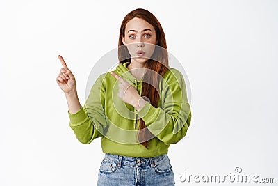 Wow awesome. Excited redhead girl gasp and look impressed, pointing fingers at uppr left corner promo, showing discounts Stock Photo