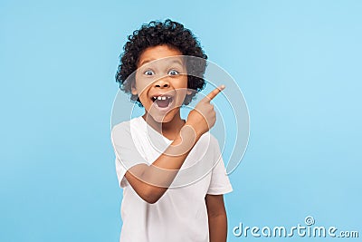 Wow look, advertise here! Portrait of amazed cute little boy with curly hair pointing to empty place Stock Photo