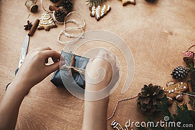 Wrapping rustic christmas gift. Hands wrapping christmas gift in stylish black paper and pine branches, cones, gingerbread cookies Stock Photo