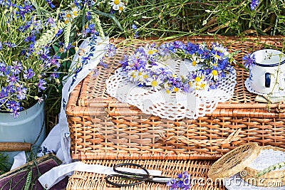 Wreath of cornflowers and chamomile on a wicker picnic suitcases in wheat field background Stock Photo